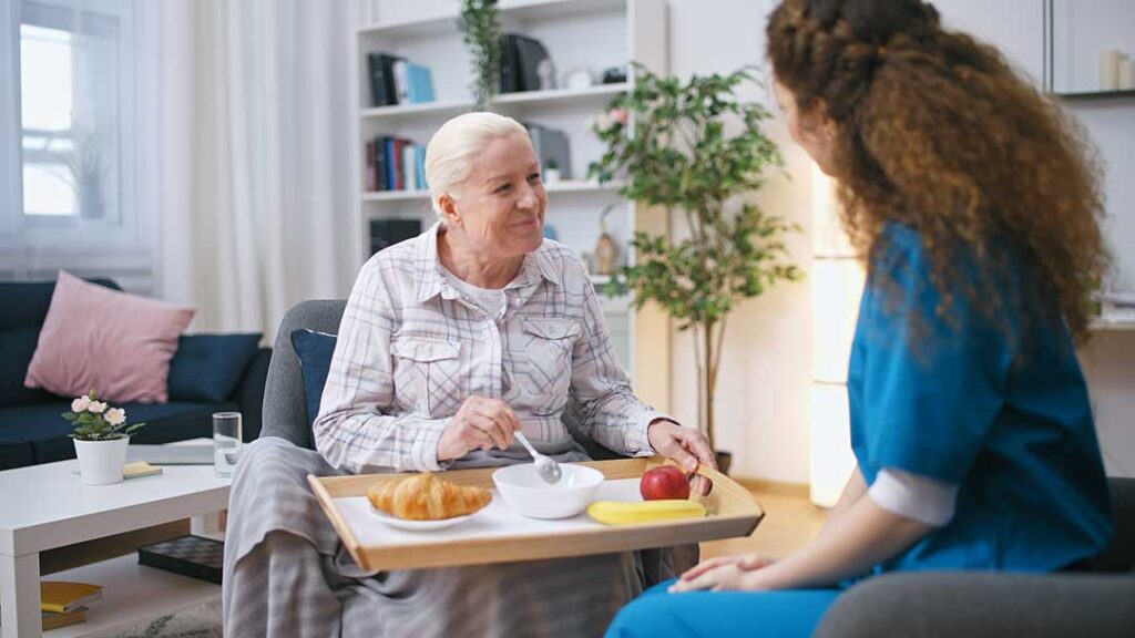 Family member sits beside an elderly resident in an assisted living room during a quiet care discussion.
